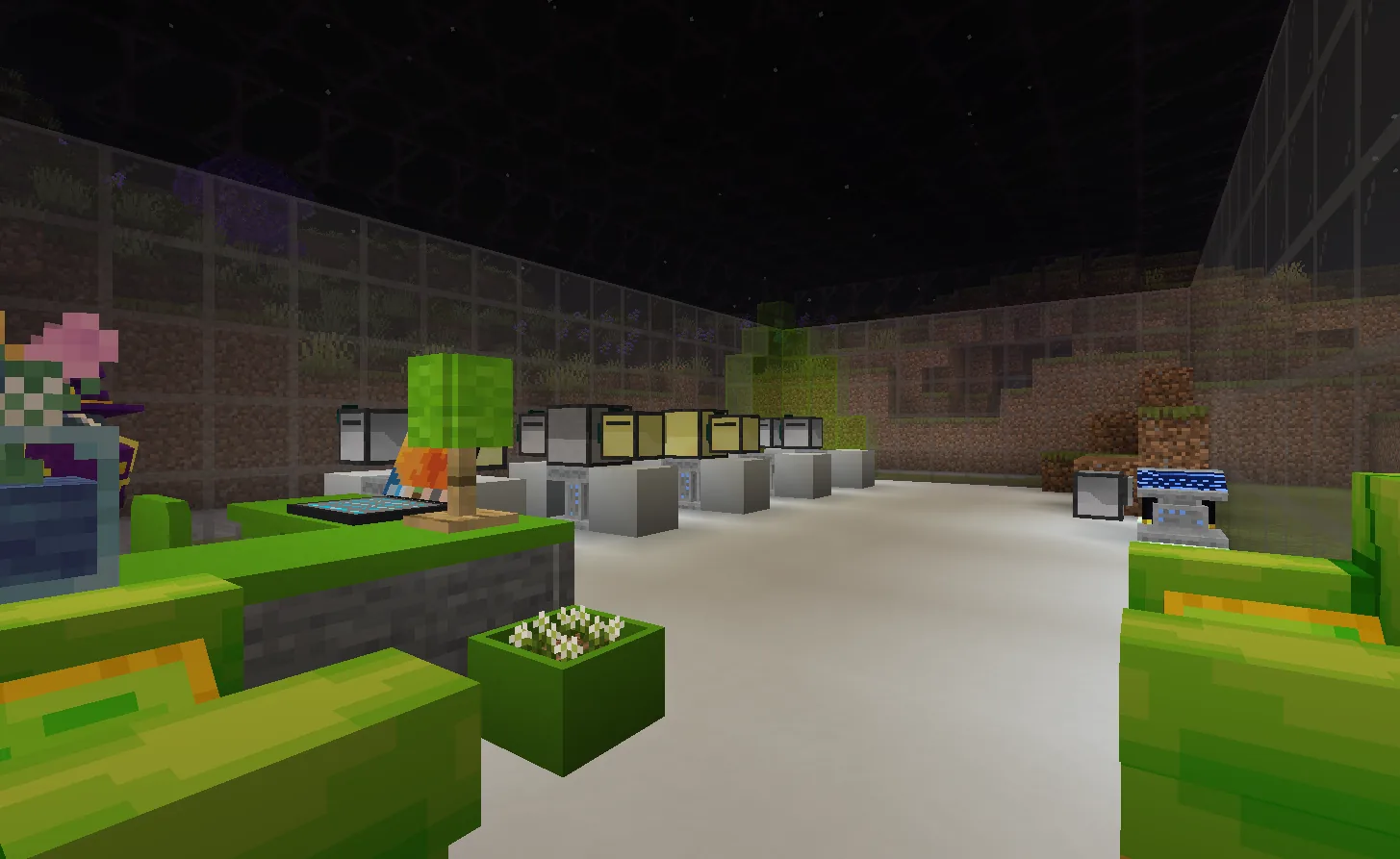 A long glass-walled room at night seen from the doorway, a double row of computers on white plinths receding into the distance, green lounge furniture in the foreground
